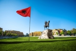 Die albanische Flagge in Tirana neben einer Statur mit blauem Himmel im Hintergrund 