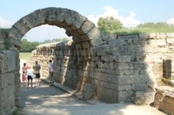 Eine Familie, welche durch einen aus Stein gemachten Bogen geht in Olympia