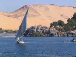 Ein Seegelboot auf dem wasser mit der Wüste von Assuan im Hintergrund