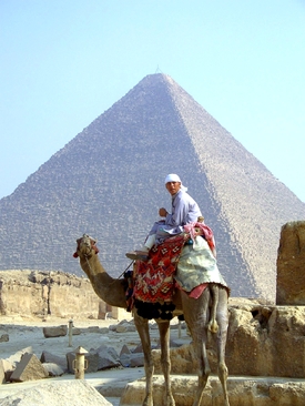 Ein Junge, welcher auf einem Kamel sitzt, welches vor einer der Pyramiden von Gizeh steht 